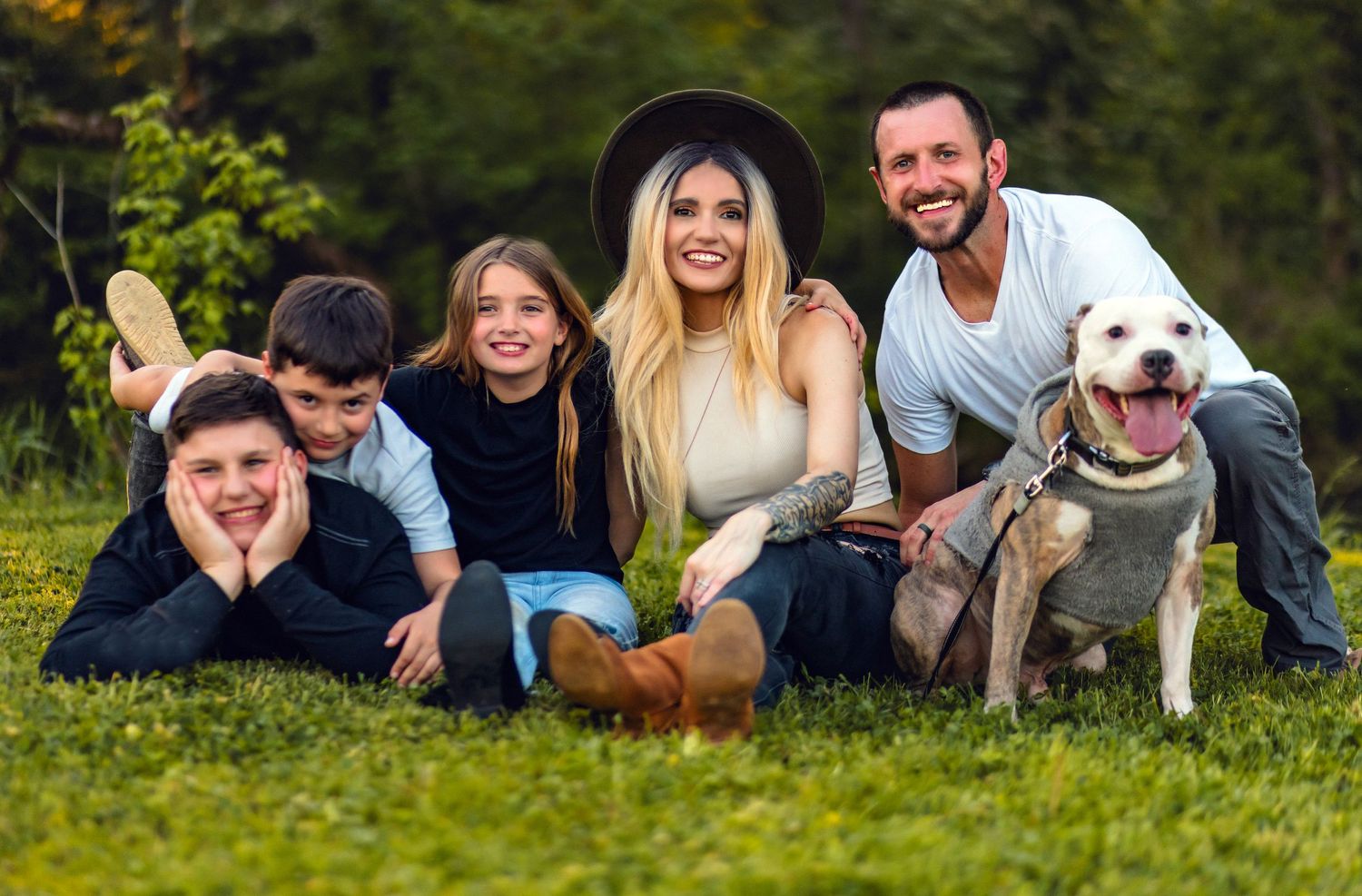 Family and white dog posing together on grass for outdoor portrait.