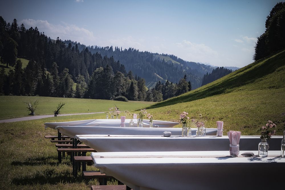 Panoramic view of a mountain landscape with wooden benches and tables overlooking a scenic valley on a sunny day.