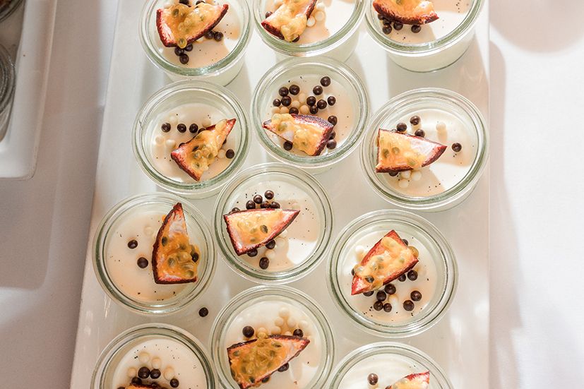 Small glass jars filled with creamy desserts topped with chocolate chips and orange garnishes arranged in neat rows.