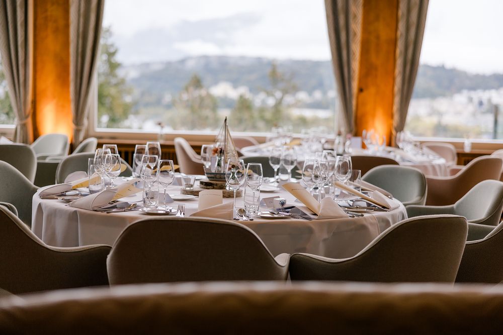 Elegant wedding reception tables set with white linens, floral centerpieces and glassware in a room with mountain views.