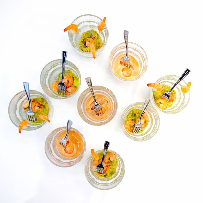 Orange-colored smoothies garnished with fruit in individual glass jars with black straws.