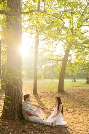 Couple sitting together under large trees in Eastern North Carolina sunlit park, holding hands in golden afternoon light.
