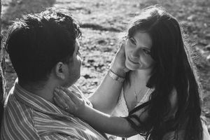 Black and white photo of a romantic couple sharing a tender moment outdoors, woman smiling and touching man's face.