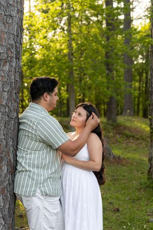 A couple shares a romantic moment in a lush green forest in Jacksonville North Carolina with the man gently touching the woman's hair.