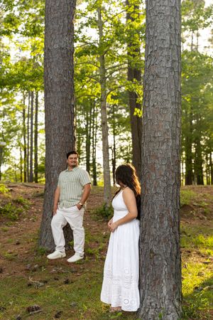 Couple posing among tall pine trees in a sunlit forest, man in striped shirt and woman in white dress. Jacksonville North Carolina