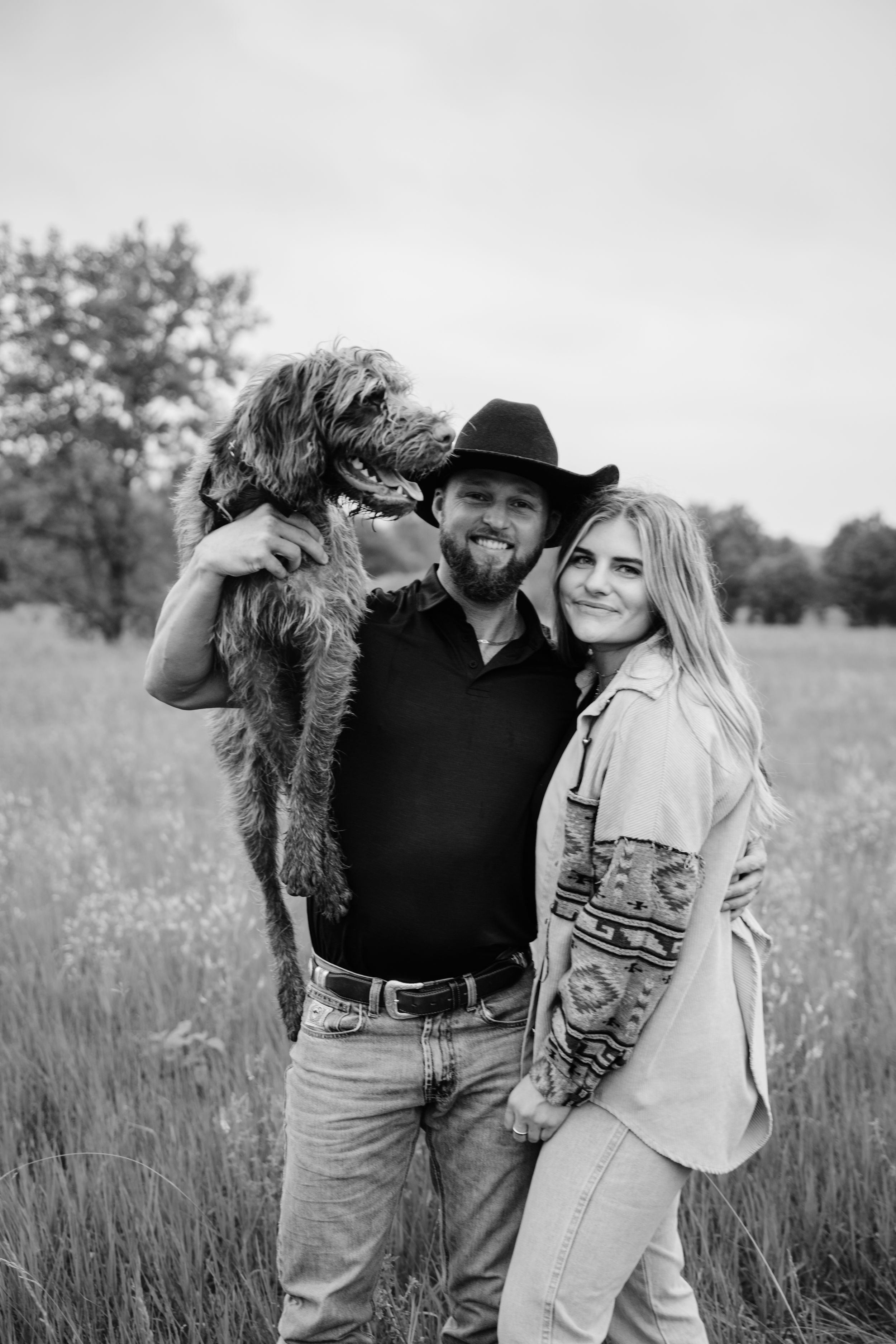 Couple embracing in a rustic field setting wearing casual western attire.