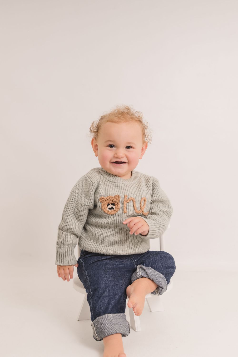 Happy toddler in grey bear sweater and jeans plays during studio photoshoot. Photographer. Hull. East Yorkshire. Photography