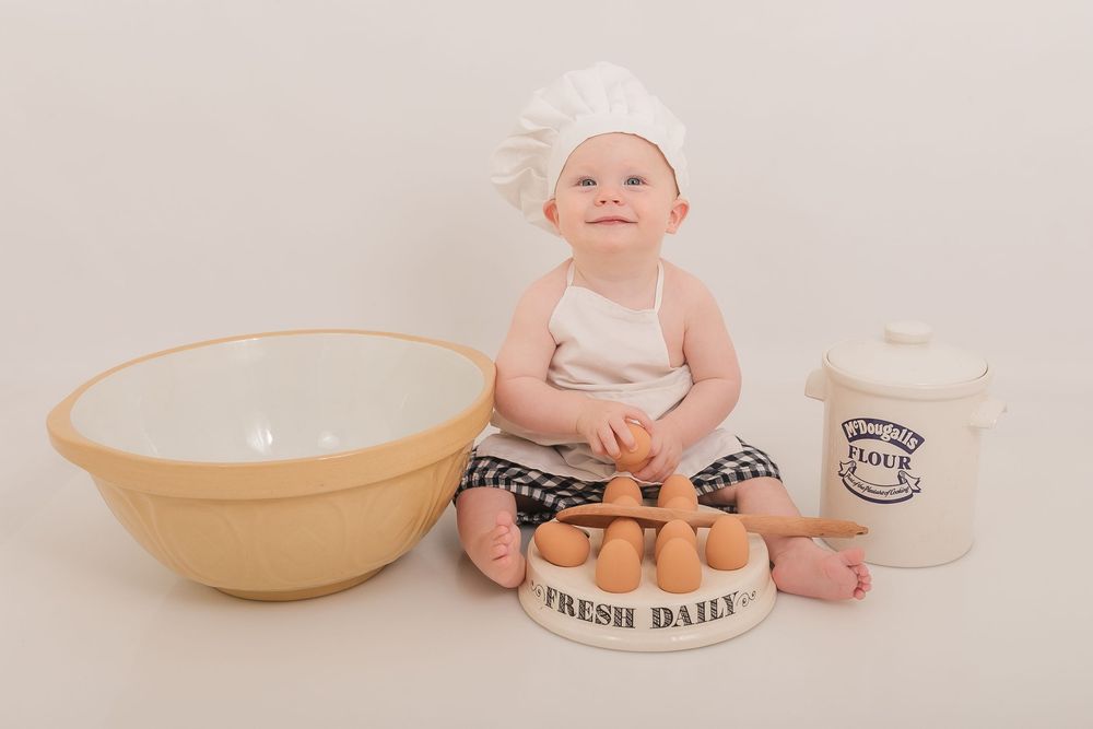Baby sits with mixing bowls and baking ingredients during a cake smash photo session. Photographer. Hull. East Yorkshire.