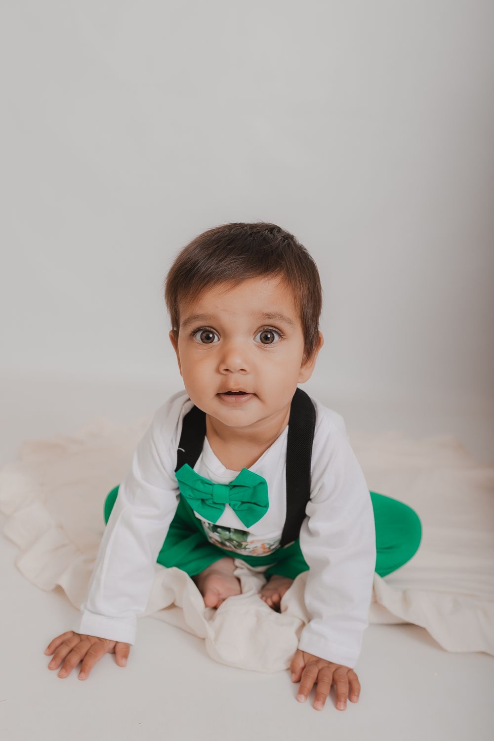 Baby in white outfit with green bowtie crawling on light background. Photographer. Hull. East Yorkshire. Photography