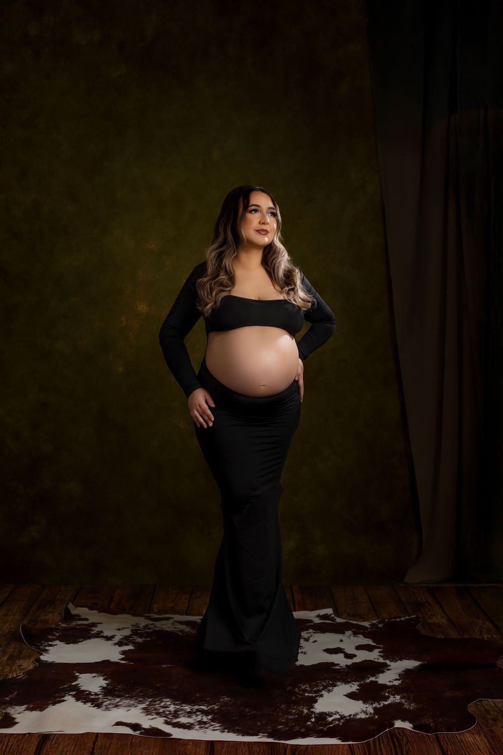 A maternity photo series showing a woman in a black dress posing against a dark backdrop with dramatic lighting.