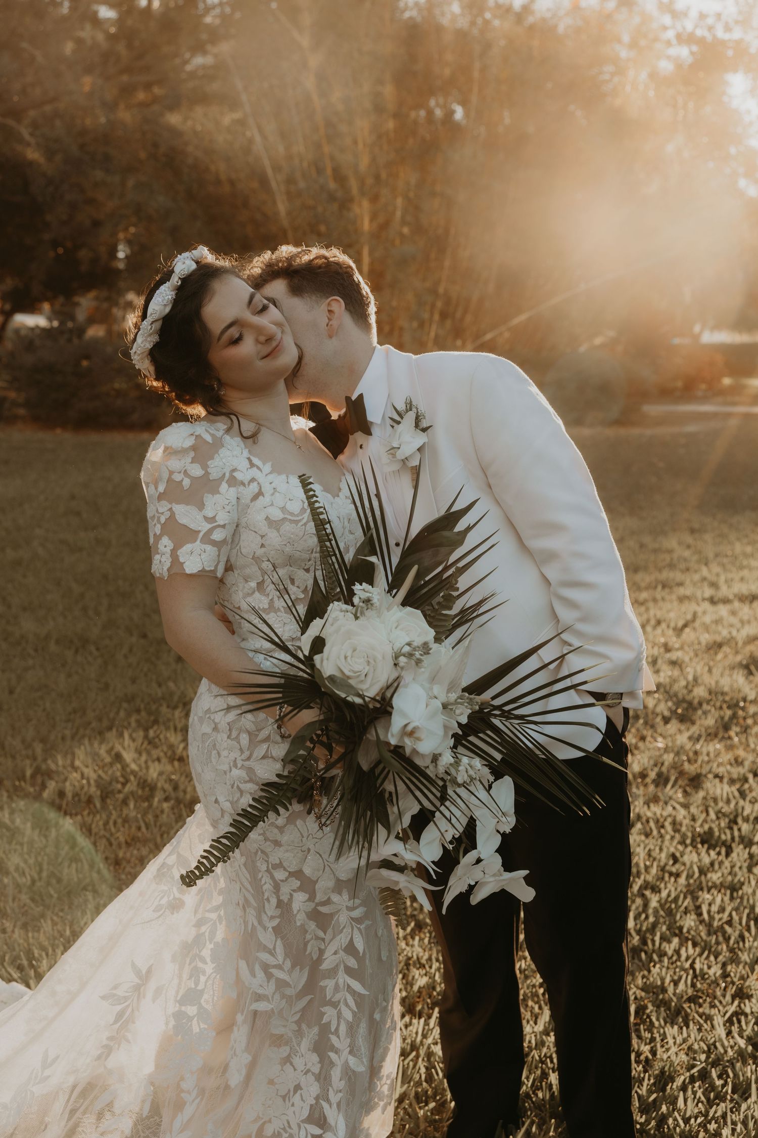 Bride in white lace gown and groom in navy suit pose back-to-back in an elegant outdoor setting.