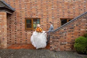 A couple shares a romantic kiss on their wedding day against a rustic brick wall backdrop.