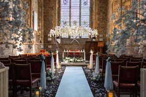 A rustic stone church interior with wooden pews and stained glass windows decorated for an elegant wedding ceremony.