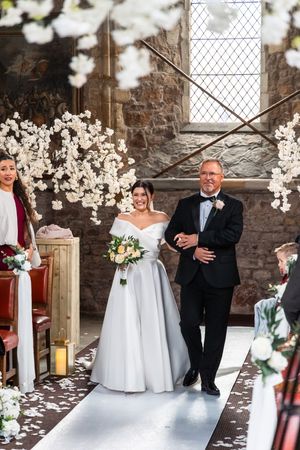 Wedding couple poses in sequence of candid shots in front of stone wall with white floral decorations and lattice windows.