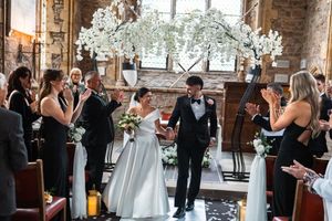 Wedding ceremony guests gathered in a rustic brick venue with elegant crystal chandeliers and floral arrangements.