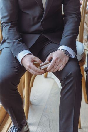 Groomsmen in dark suits sit in wooden chairs showing their matching dress socks.