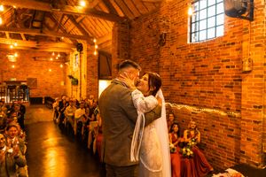 Romantic wedding ceremony in rustic brick venue with warm amber lighting and exposed wooden beams.