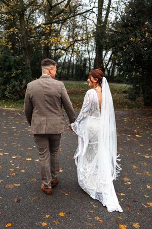 Couple walking along autumn path with fallen leaves and trees.
