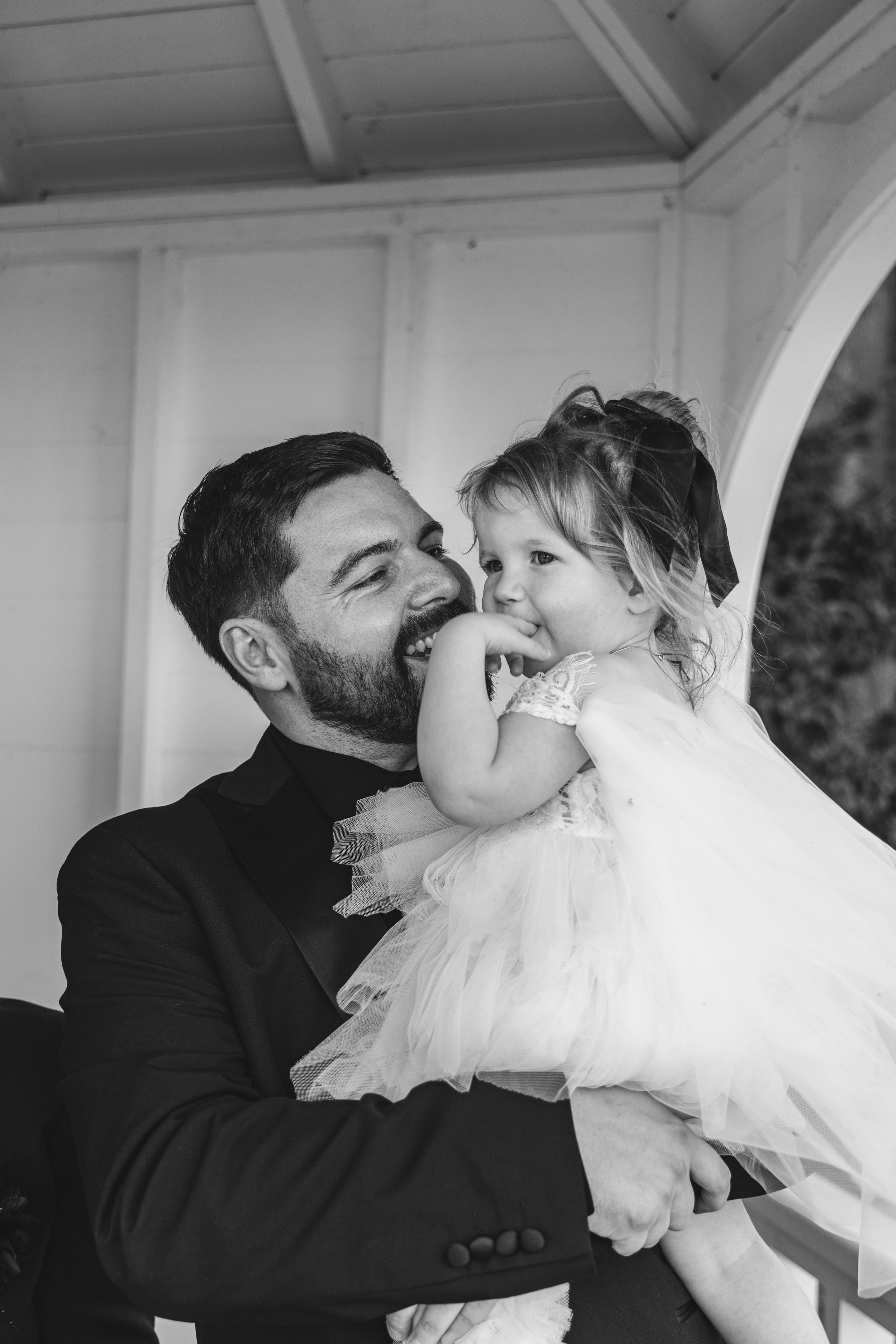 A touching black and white candid moment between a well-dressed adult and joyful child in a white dress.