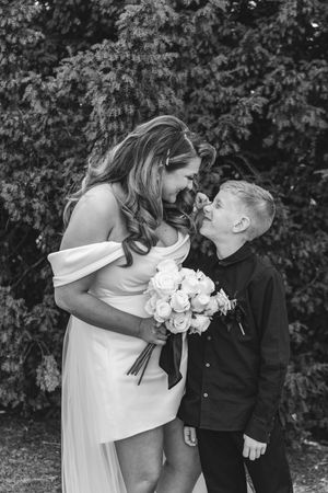 A monochrome moment captured at a spring wedding with a white dress and bouquet against lush foliage backdrop.