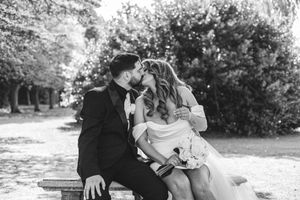 A romantic black and white moment captured on a park bench surrounded by lush greenery on a sunny day.