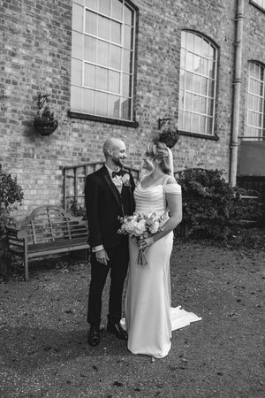 A bride and groom share a tender moment outside a historic brick building with large windows.