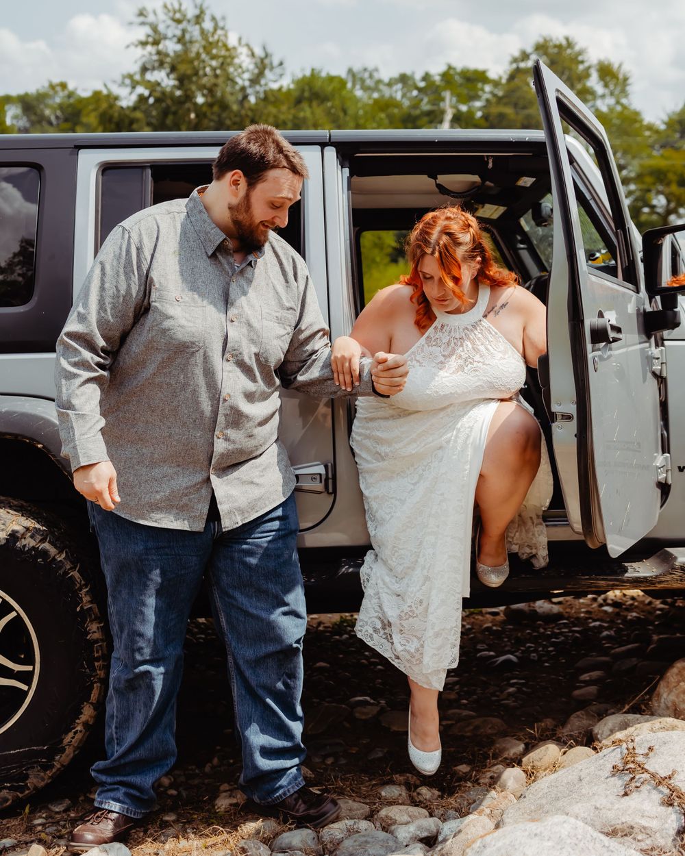 Couple exiting a grey Jeep Wrangler parked on rocky terrain.