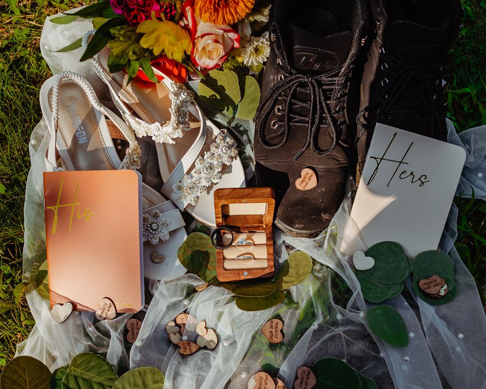 Wedding details including hiking boots, rings, and floral elements arranged on grass.