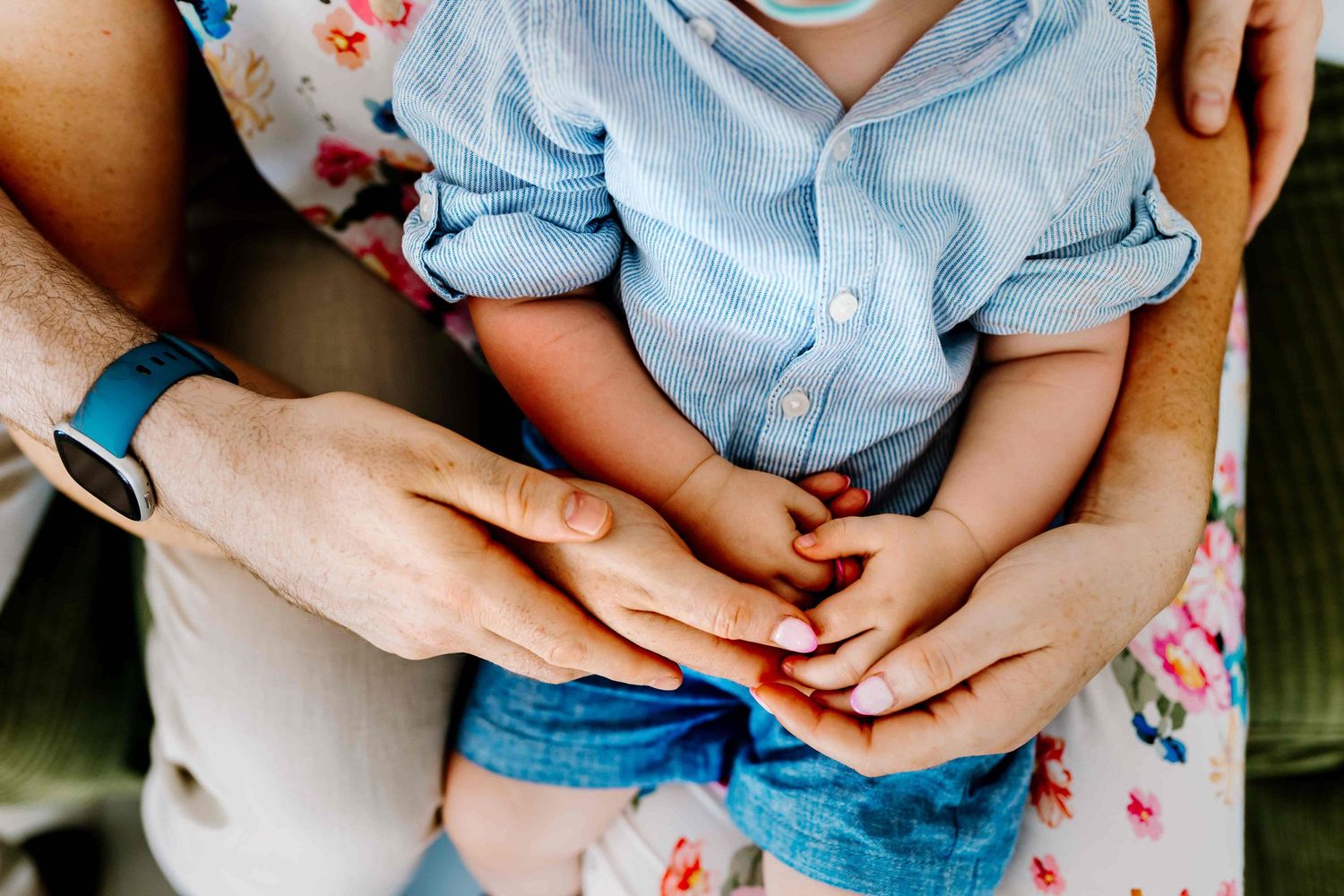 Father, mother, and their baby gently touch hands, creating a tender family moment.