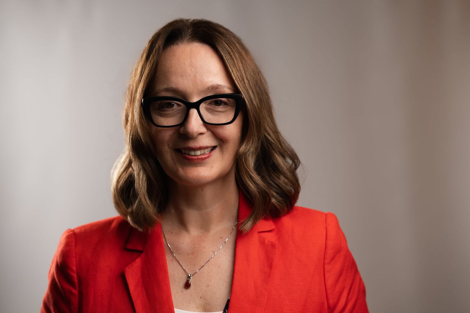 Smiling woman with curly dark hair and glasses wearing a black sleeveless top with arms crossed.