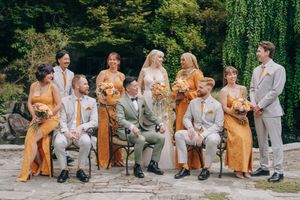 Wedding party seated on stone wall wearing coordinated grey and mustard yellow attire.