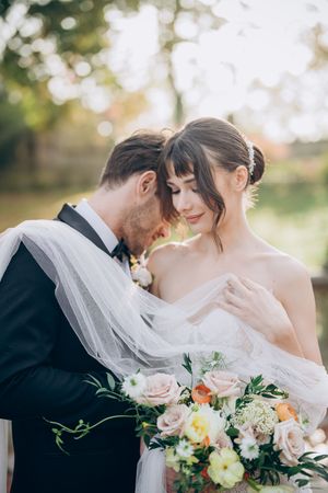 Romantic outdoor wedding portrait with soft bokeh background and floral bouquet.
