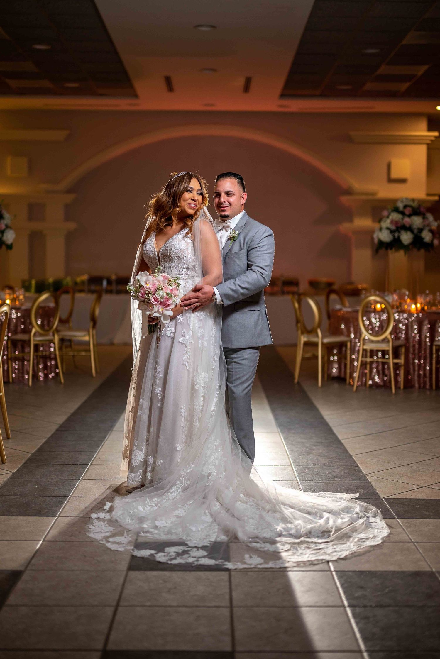 Wedding couple poses for romantic portrait in elegant ballroom with decorative lighting.