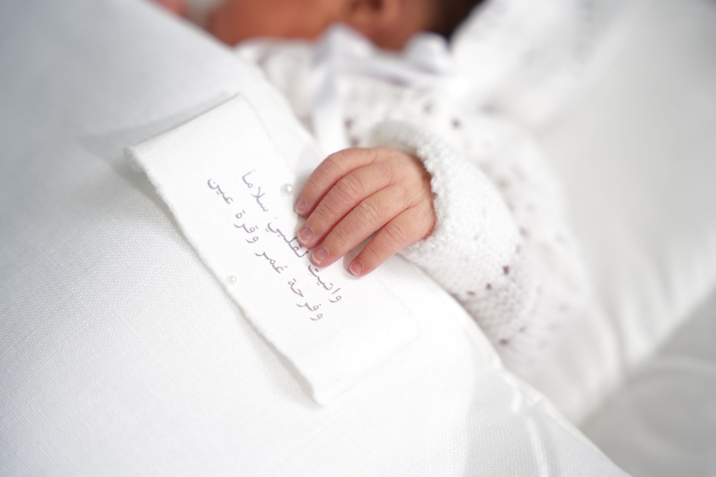 Close up shot of small hand holding handwritten note on white fabric.