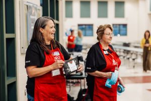 Two volunteers in red aprons coordinate at community service event.