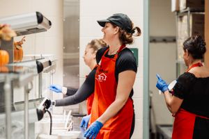 Volunteer in red apron and gloves working in kitchen area.