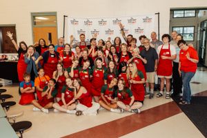 Large group wearing red aprons posing together at community event.