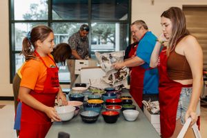 People preparing food together at cooking station with multiple ingredient bowls.