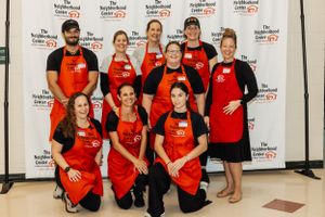 Group of volunteers in red aprons pose together for team photo at charity event.