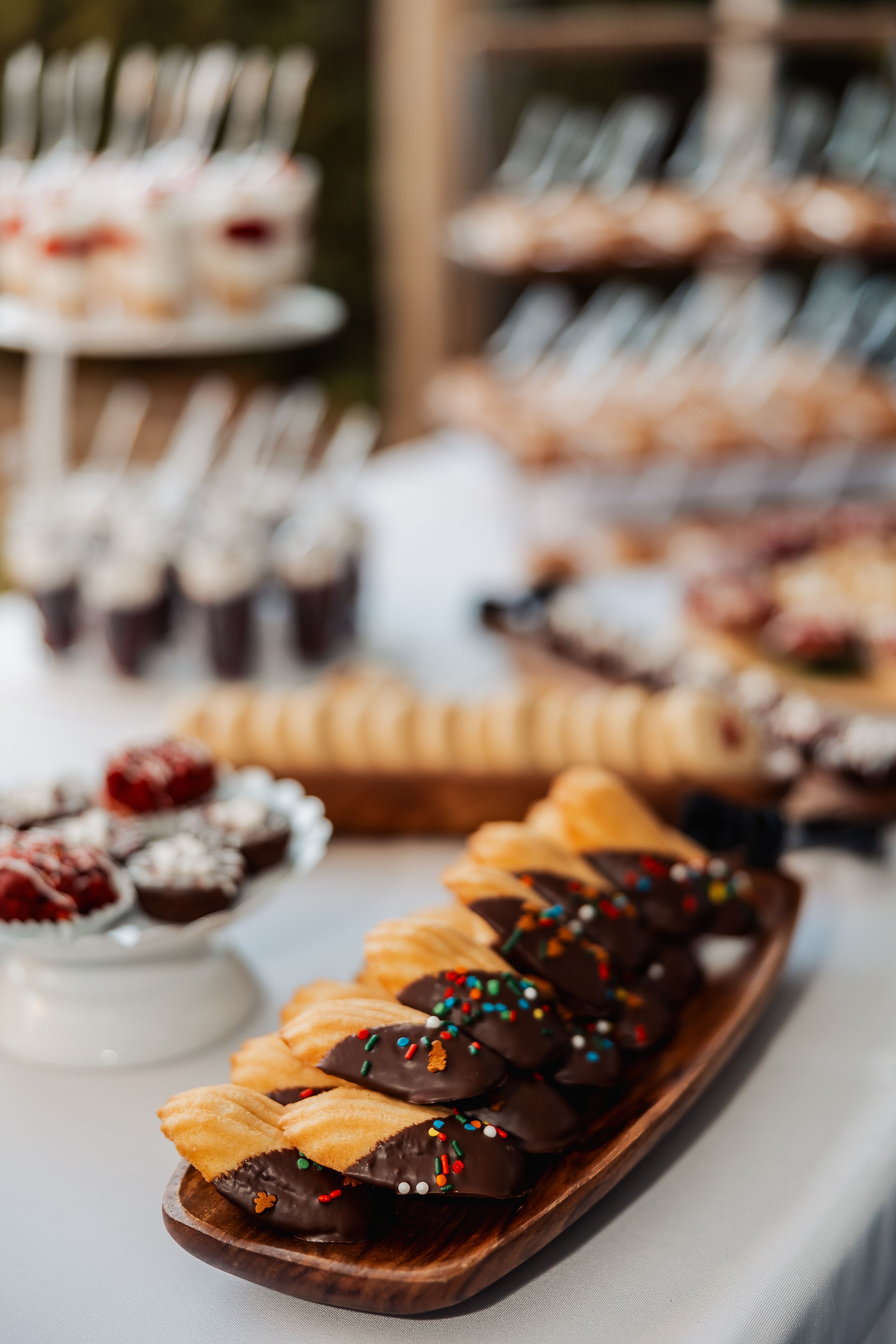 Chocolate dipped pastries with sprinkles arranged on wooden serving board at dessert table.