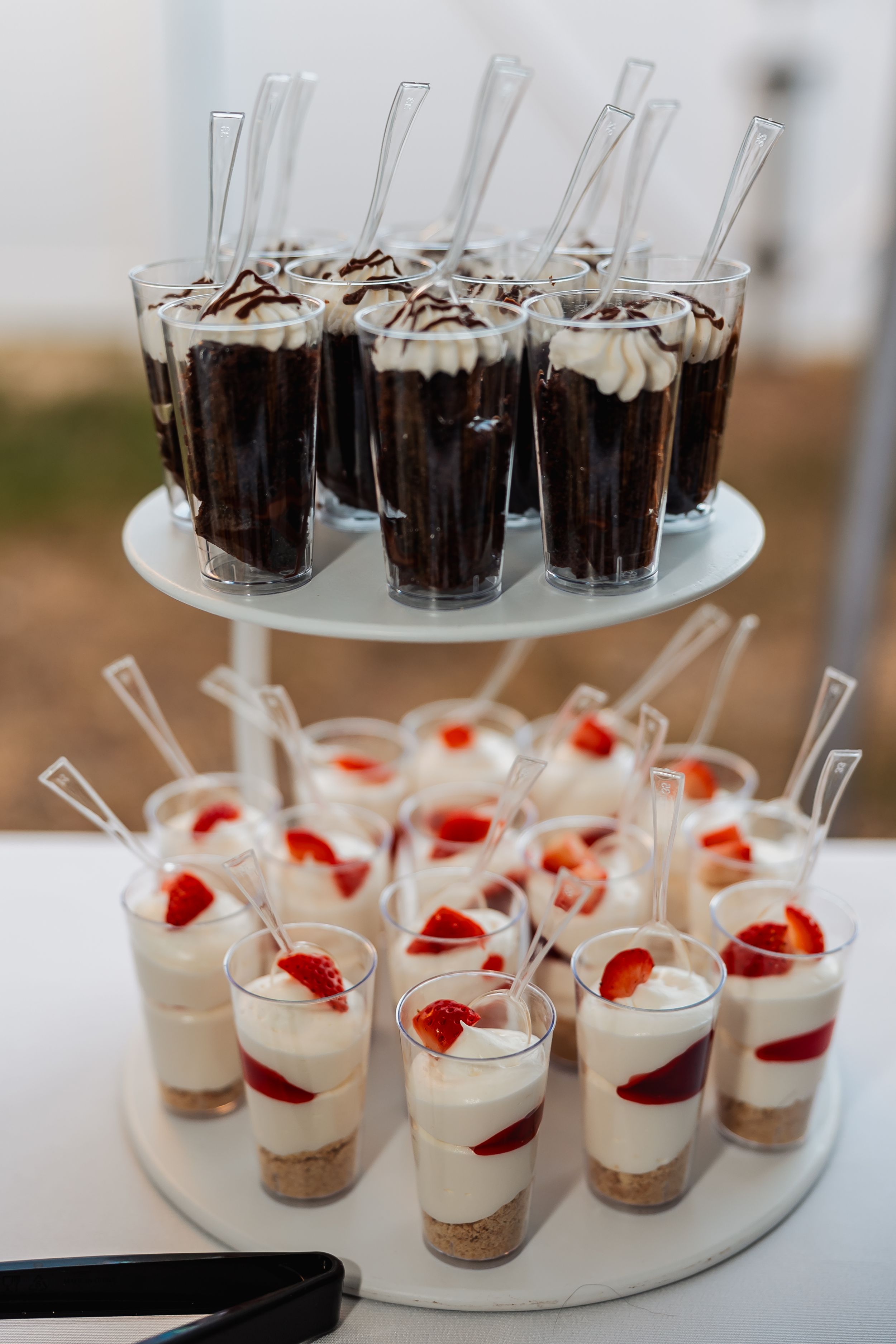 Tiered dessert display with chocolate mousse and strawberry parfaits in glass cups.