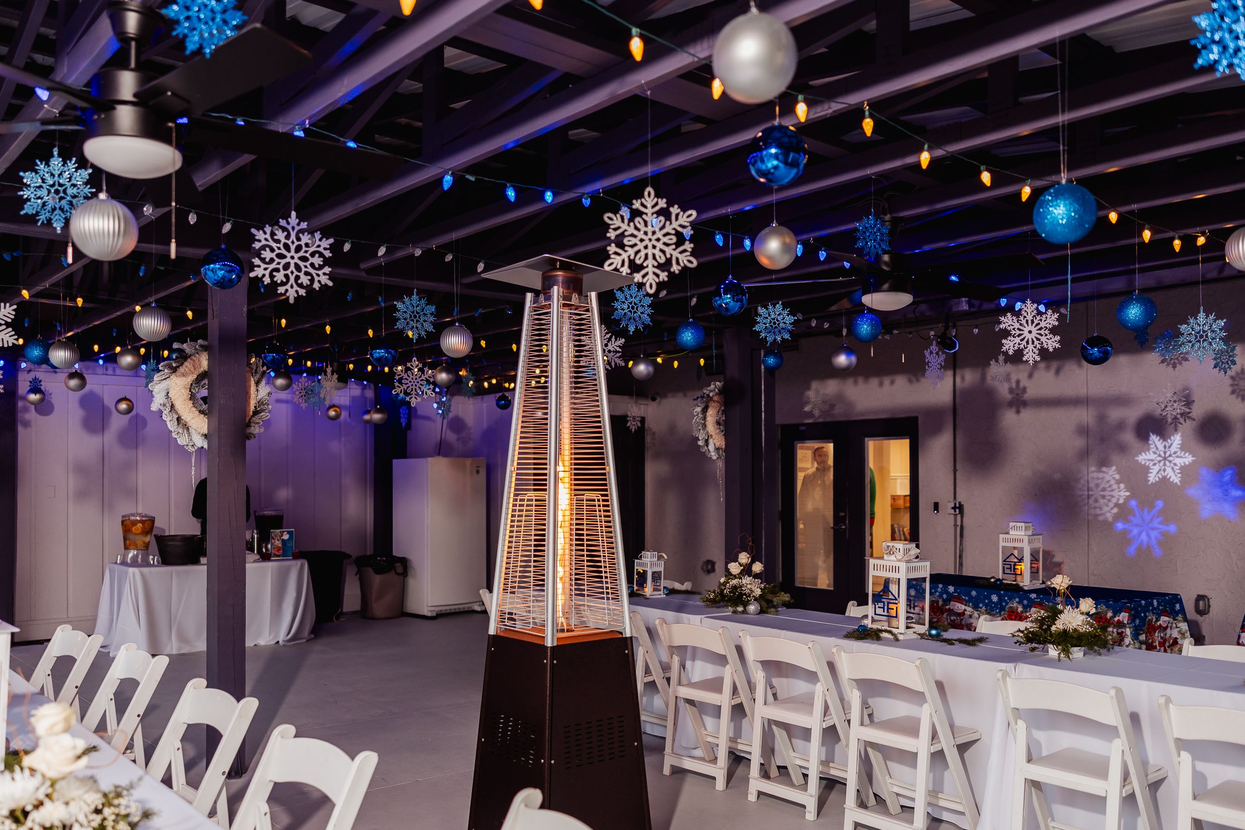 Indoor event space decorated with hanging snowflakes, string lights and white chairs.