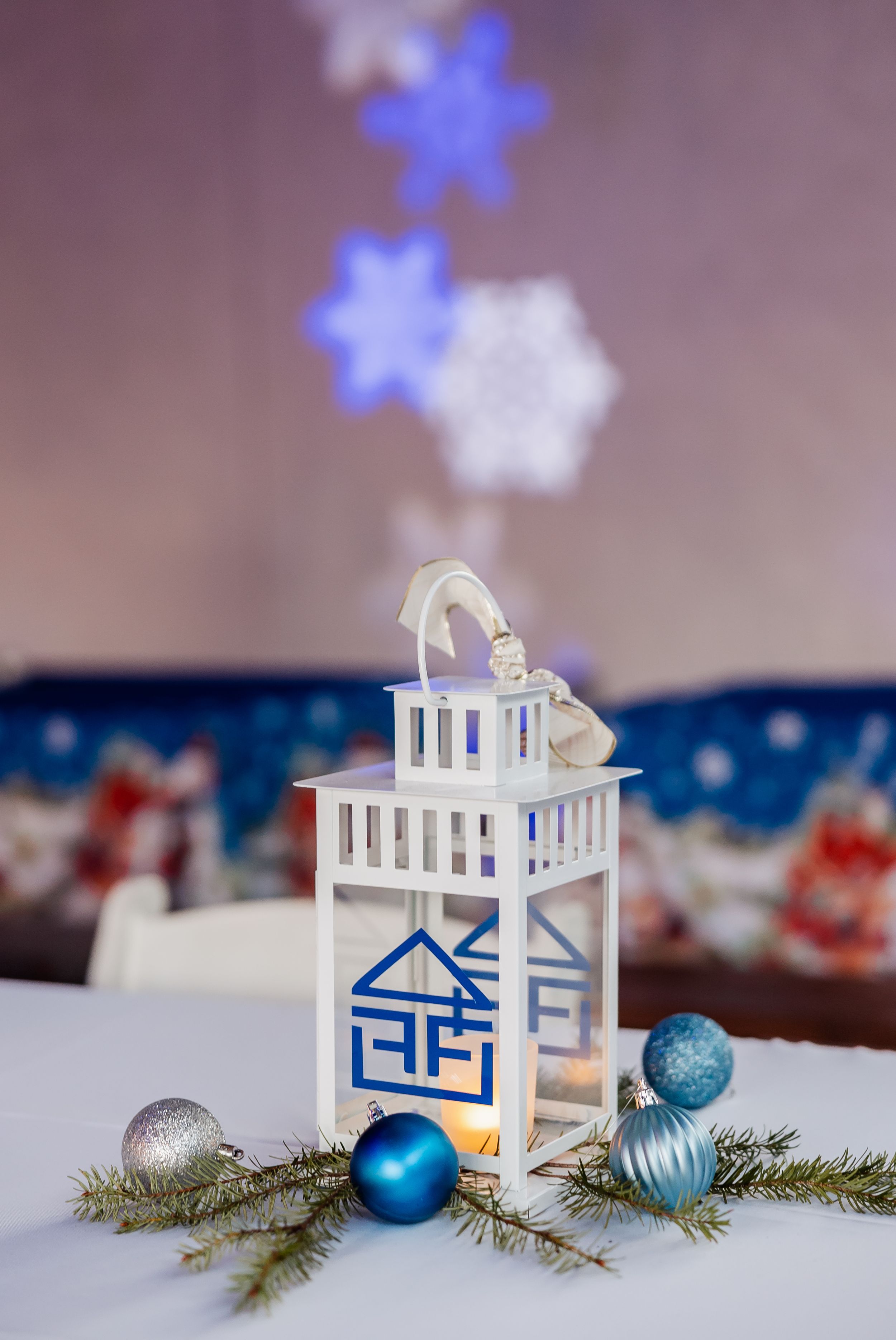 White decorative lantern with blue logo and winter ornaments on white tablecloth.