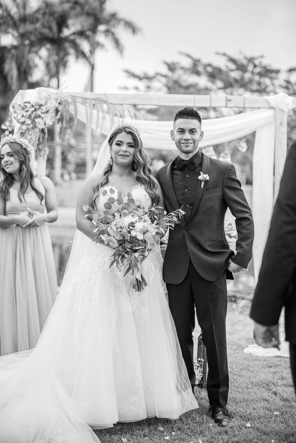 A happy couple poses after their outdoor wedding ceremony with white floral arrangements.