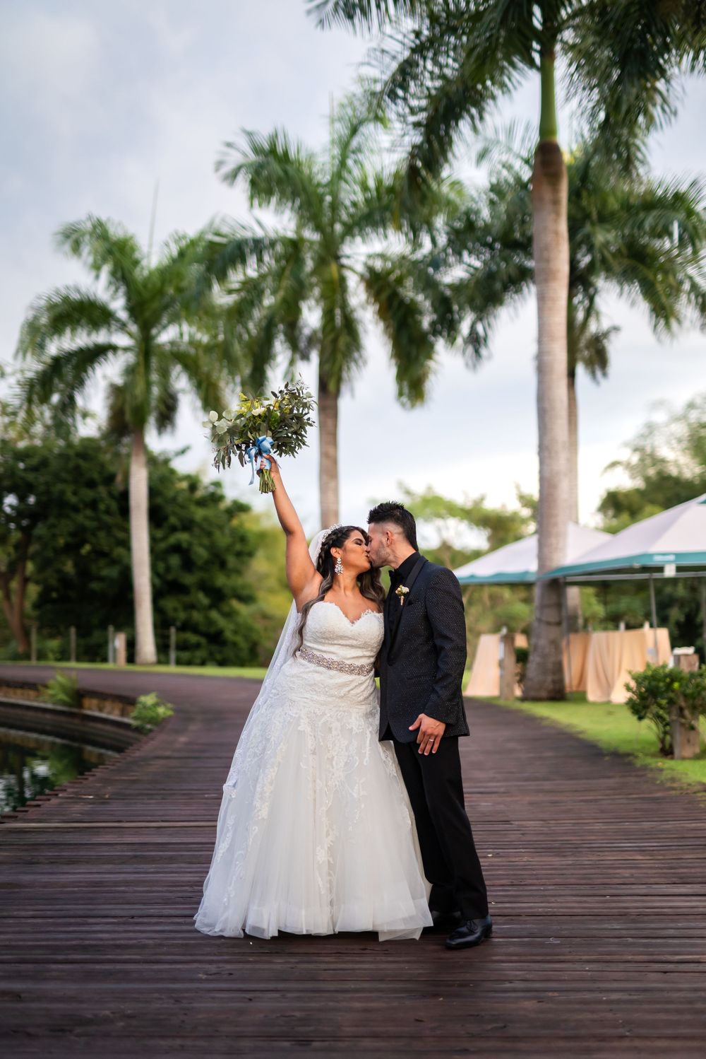Newlyweds celebrate on wooden boardwalk with tall palm trees in background.