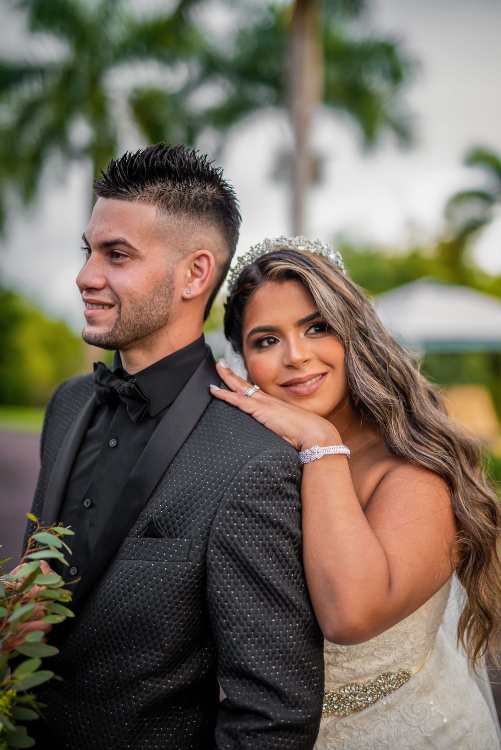 Close portrait of newlyweds in formal attire against tropical garden setting.