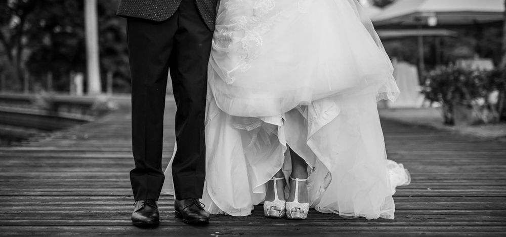 Black and white detail shot of bride and groom's feet on wooden boardwalk.