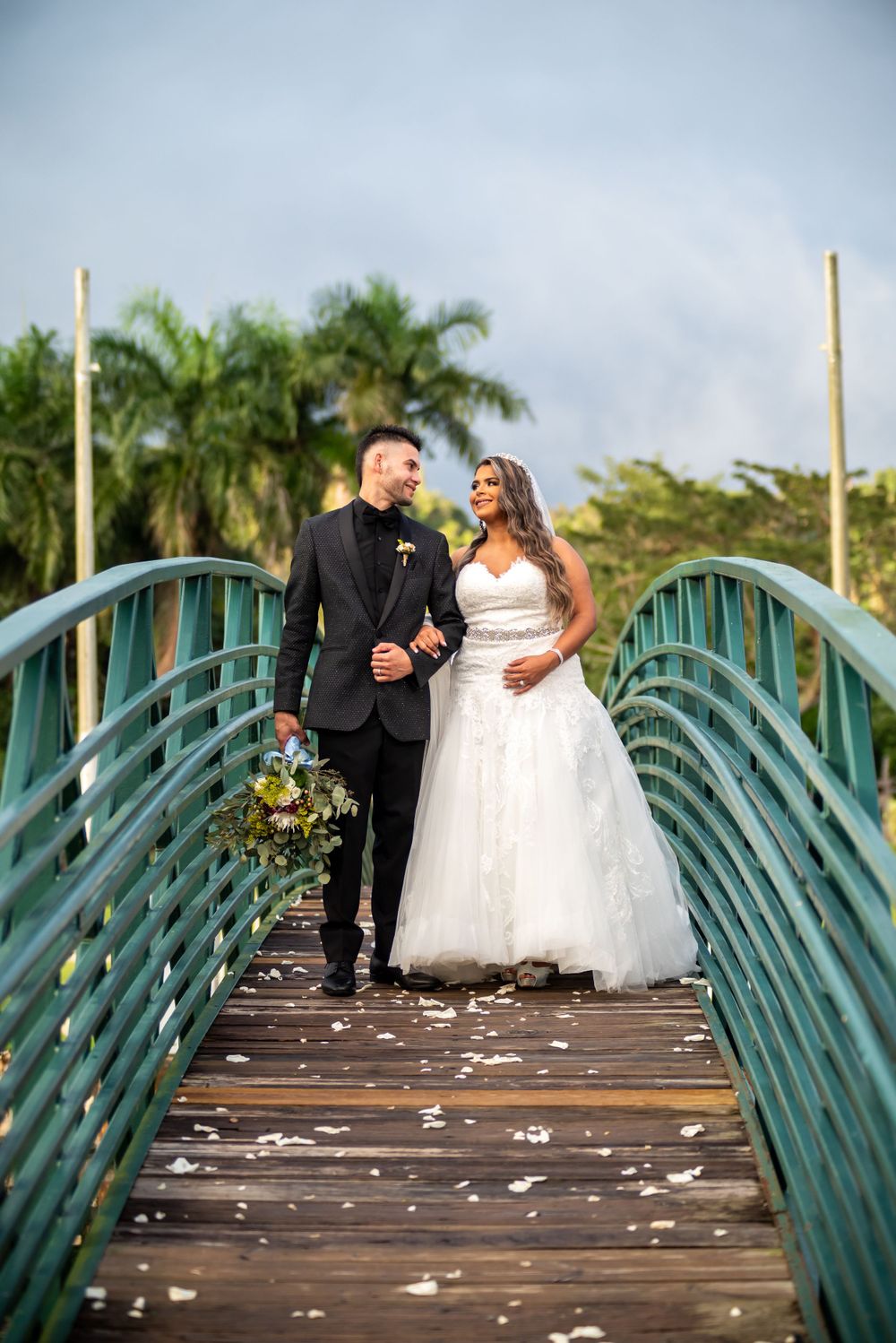 A couple shares a romantic moment on a turquoise bridge with palm trees in the background.