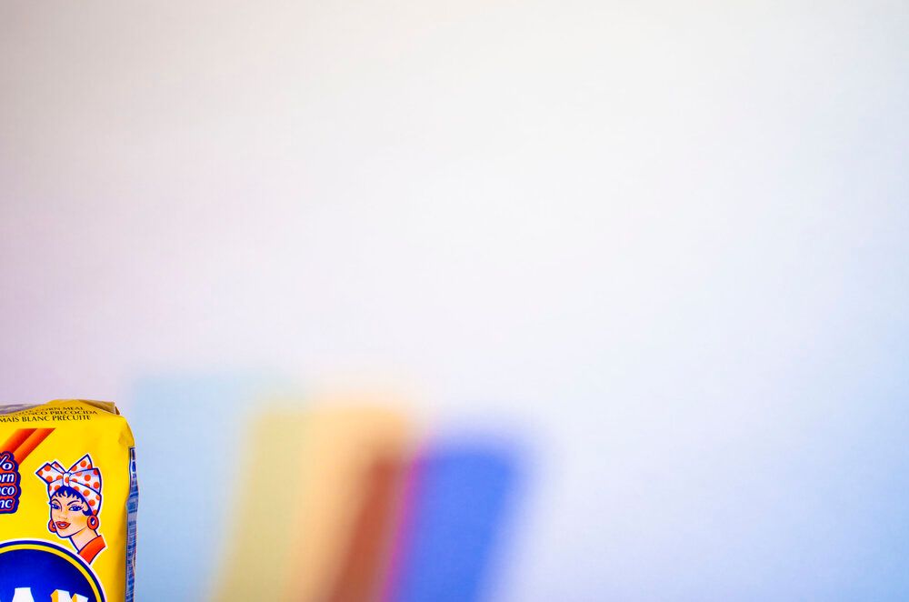 Blurred colorful background with corner of Harina Pan product package visible in foreground.
