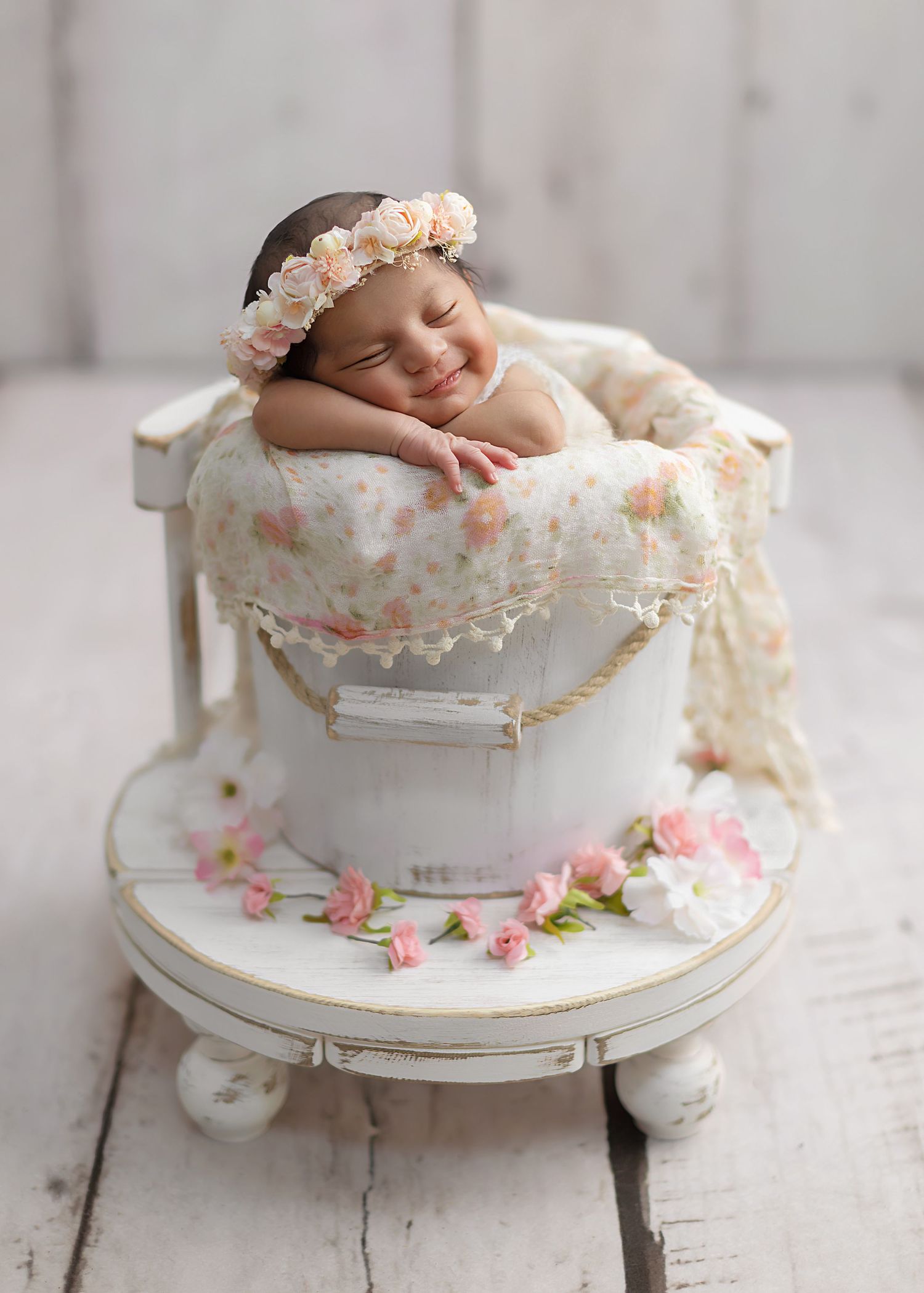 A smiling baby in a bucket pose with white backdrop. boho chic style. flowery magical pretty girl.